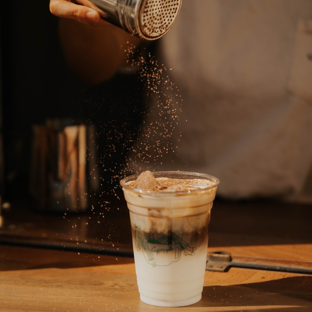 Iced coffee dusted with cocoa powder in a branded Café Maud cup