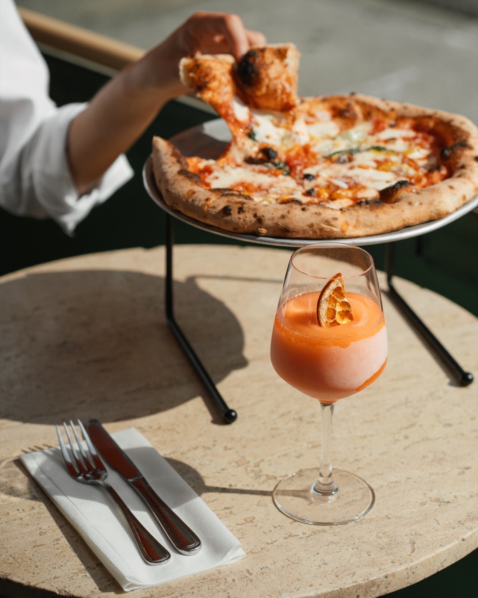 Personal pizza and a frozen Aperol Spritz on an outdoor table during Café Maud happy hour